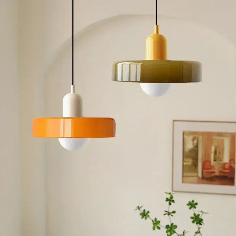 Two modern glass led macaron pendant lights in orange white and mustard off-white hang from black cords on wall