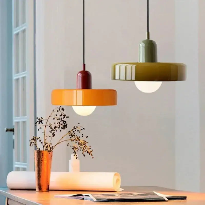 Two modern glass led macaron pendant lights in orange and olive green with black cords above a wooden table