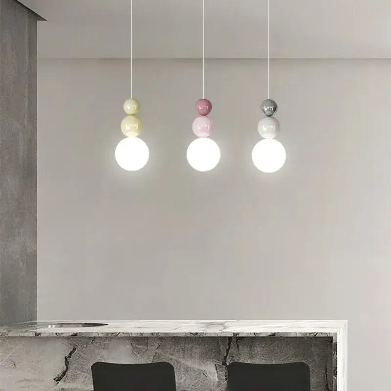 Three modern metal pendant lights with stacked globe design in pastel yellow pink and matte gray light color options