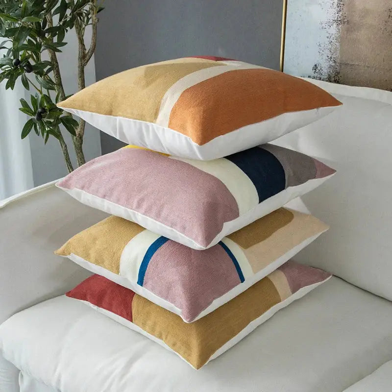 Stack of four modern pastel geometric cushion covers with bold horizontal stripes in soft earth tones and textured fabric