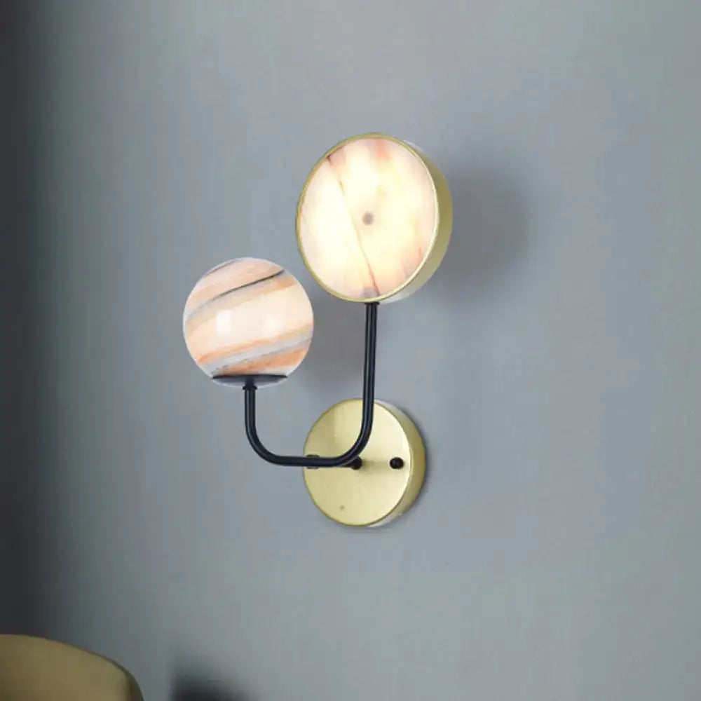 Modern peach and cream glass sconce light bedroom fixture with two spherical glass shades on brass base and black arm inches fixture