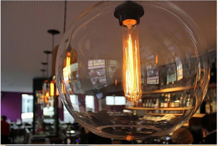 A warm glowing edison-style bulb in a clear spherical glass globe modern pendant light for bedroom dining room decor