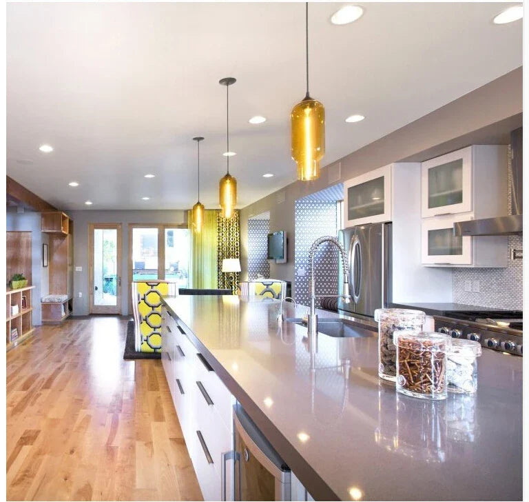 Gold-toned modern pendant lights with sleek cylindrical design hang above kitchen island for loft and dining room decor