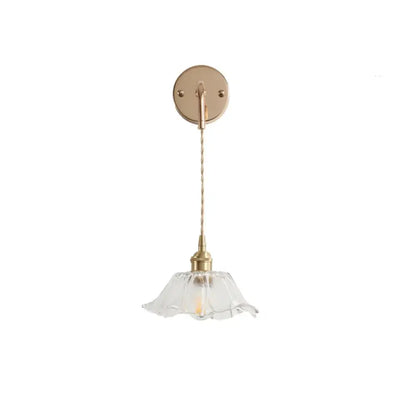 A modern brass-finished wall light with decorbites clear glass petal-shaped shade and clear glass led bulb