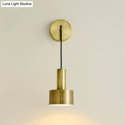 Brass-finished minimalist wall sconce with cylindrical shade and black cord for modern pink and brass bedside reading e14 e26 e27