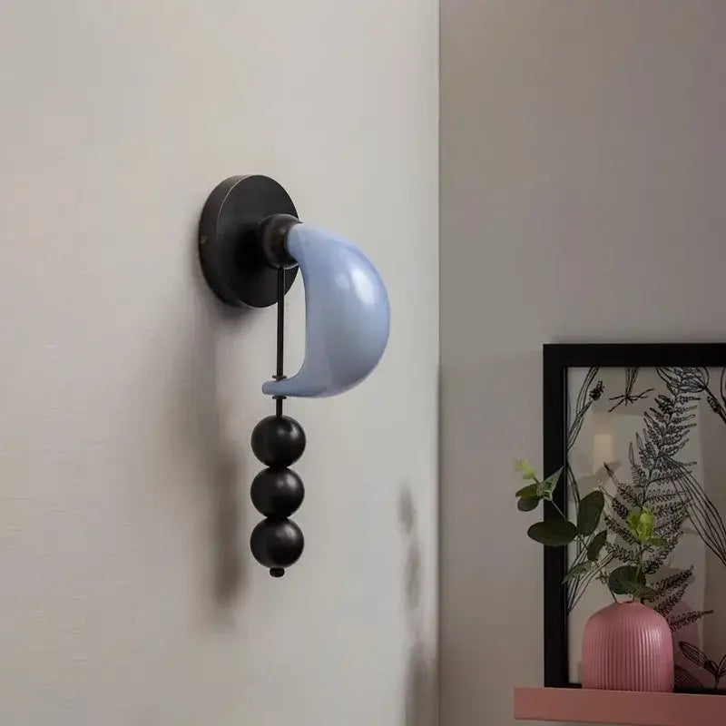 A modern wall lamp featuring a matte black base and light blue crescent shade with decorbites brass curve glass accents
