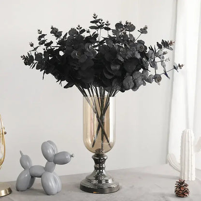Elegant black eucalyptus flower arrangement in a tall clear glass vase with metallic base for modern living room decor