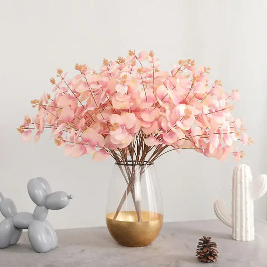 A clear glass vase with a gold-finished base holds a modern pink eucalyptus flower arrangement for living room decor
