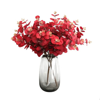 A vibrant red eucalyptus flower arrangement in a translucent gray glass vase for modern living room decor
