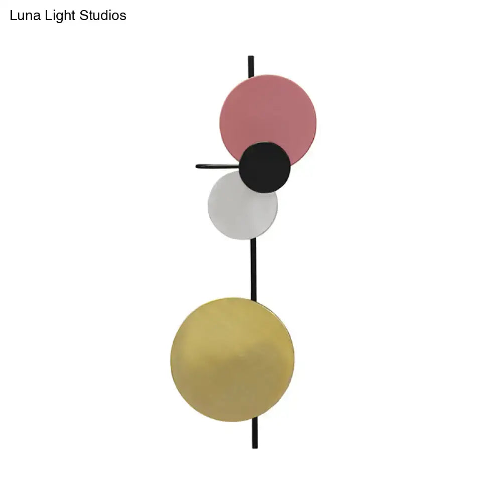 Modern abstract wall sconce featuring three stacked circular discs in matte pink, black, and white, with a brushed gold lower disc mounted on a sleek black rod.