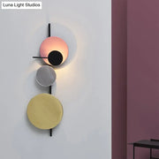 Modern wall light with three stacked circular matte pink silver and gold shades on black metal frame for white yellow bedroom lighting