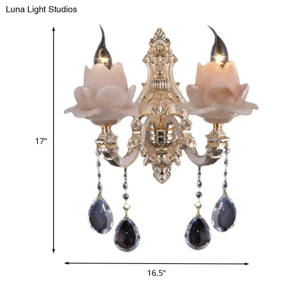 Gold-toned ornate wall lamp with pinkish milky glass lotus shades and dangling dark teardrop crystal accents for bedroom use