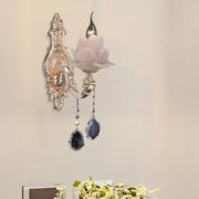 Elegant silver-toned wall lamp with pink milky glass lotus shade and dark teardrop crystal accents for bedroom sconce