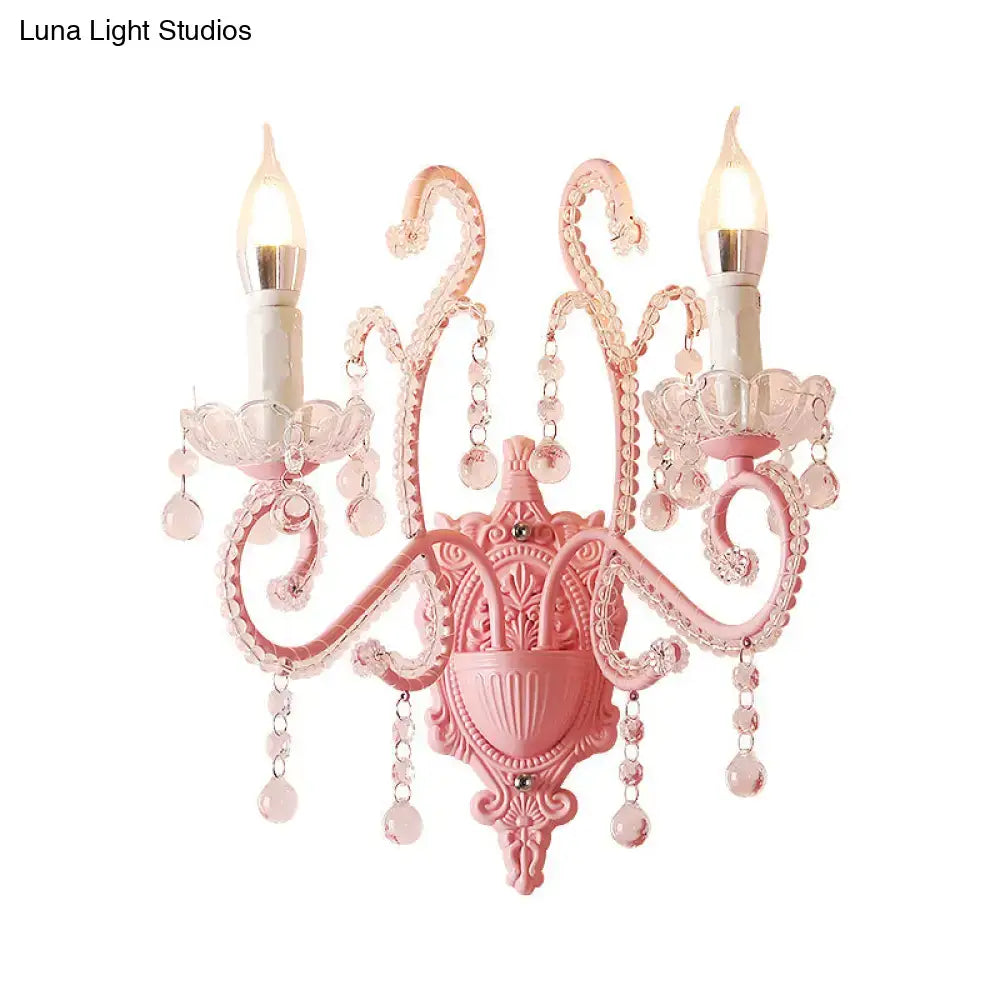 Modern pink metallic scroll arm wall lamp with ornate design crystal droplets and two candle-style bulbs for bedroom use