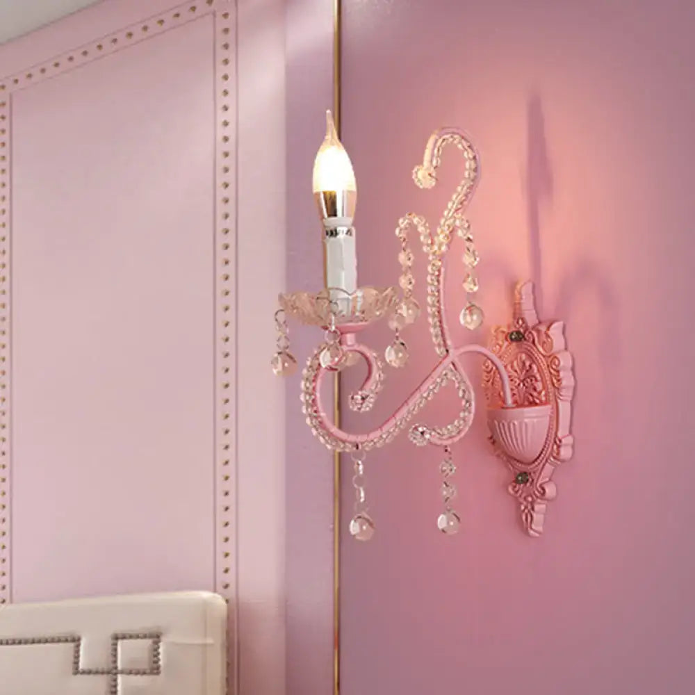 Modern pink metallic scroll arm wall lamp with crystal accents and candle-style bulb for bedroom sconce lighting