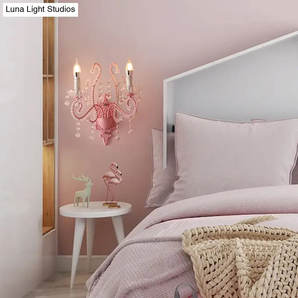 Modern pink metallic scroll arm wall lamp with crystal and two candle-like bulbs for elegant bedroom lighting