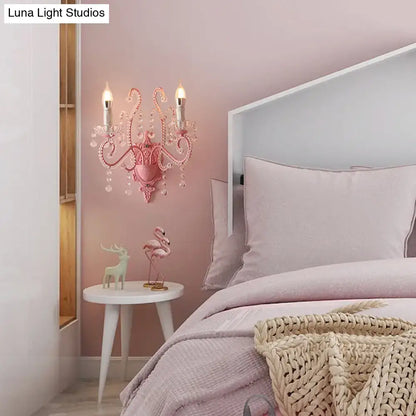 Modern pink metallic scroll arm wall lamp with crystal and two candle-like bulbs for elegant bedroom lighting