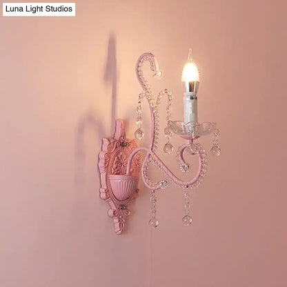 Modern pink metallic scroll arm wall lamp with crystal droplets and candle-style bulb for elegant bedroom sconce lighting