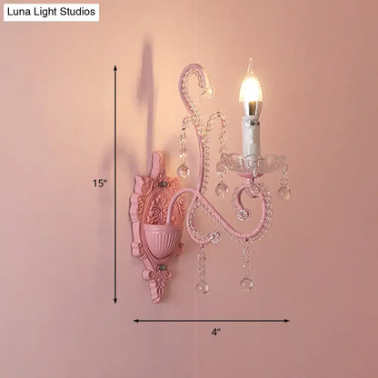 Modern pink metallic scroll arm wall lamp with ornate crystal droplets and candle-style bulb for bedroom sconce lighting