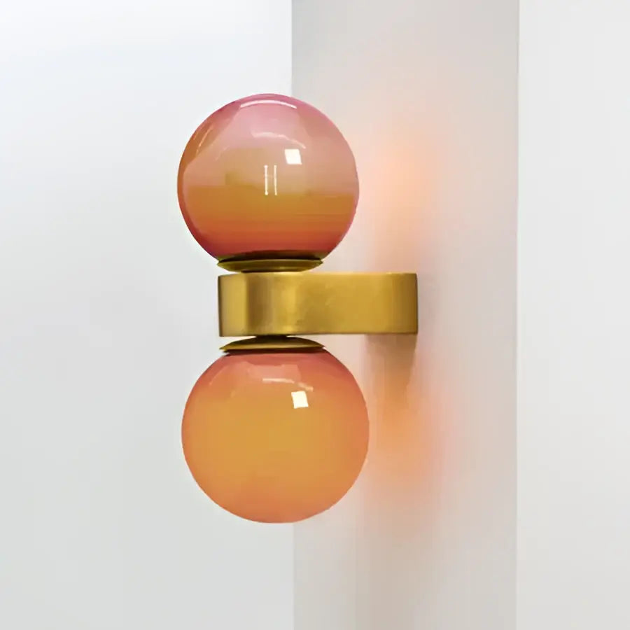 A modern wall lamp with two gradient pink to orange decorbites glass ball led spheres on a polished brass bracket