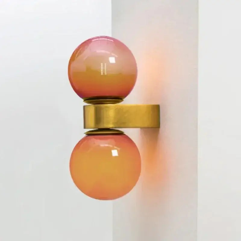 A modern wall lamp featuring two glossy pink and orange glass ball led spheres connected by a brass bar decorbites glass ball
