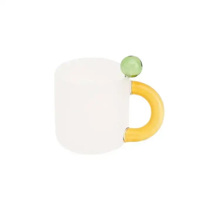 A frosted white ceramic mug with a yellow handle and green bead in a modern pink and red glass mug set