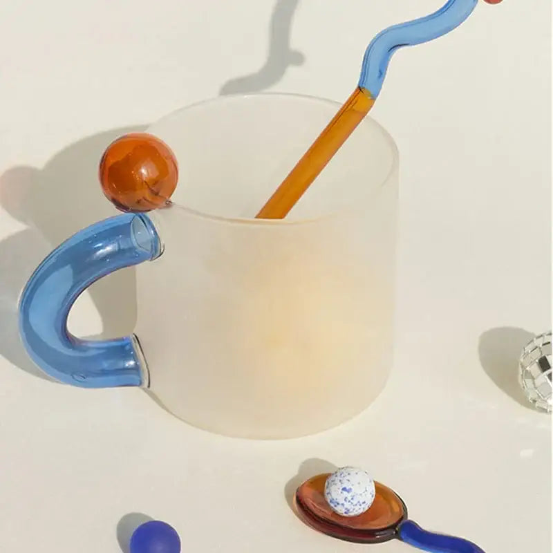 A frosted glass mug with a vibrant blue curved handle and orange accent in a modern glass mug set