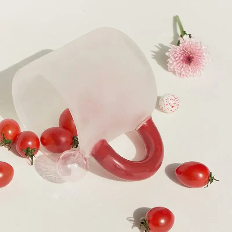 Translucent frosted glass pitcher with glossy red handle and spout filled with cherry tomatoes in glass mug set