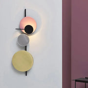 Modern wall mount light with three stacked pink silver and gold circular discs in black metal for living room use