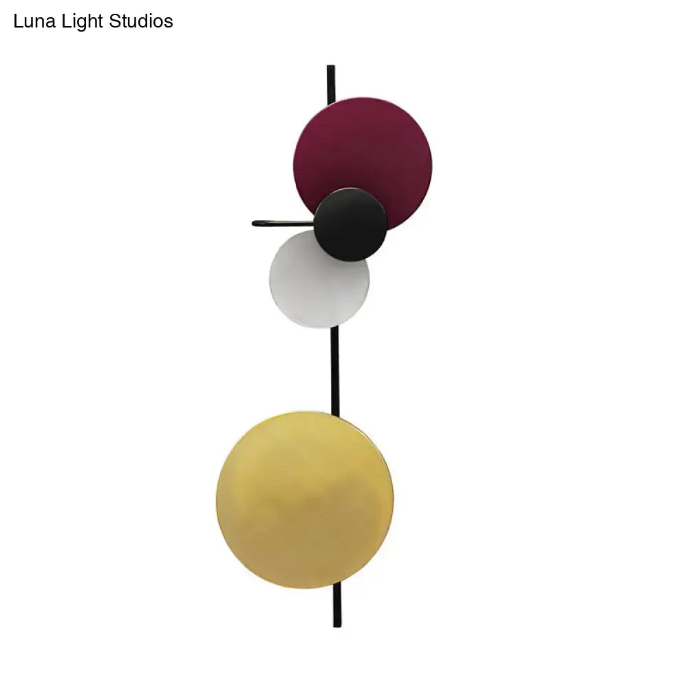 Modern circular wall mount light with burgundy, black, white, and gold discs on black rod for living room use