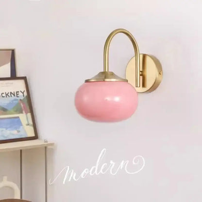 A sleek pink glass ball wall lamp with polished brass arm and mounting plate for living room decorbites glass ball lighting