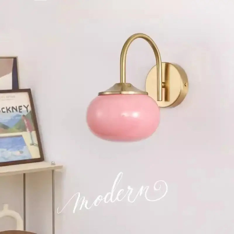 A sleek pink glass ball wall lamp with polished brass arm and mounting plate for living room decorbites glass ball lighting