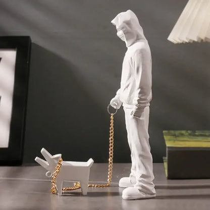 White resin decorbites dog sculpture featuring a hooded figure holding a gold chain leash with matching dog accessory