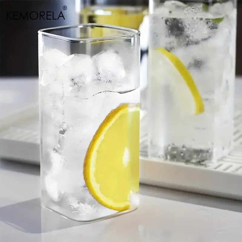 Modern rectangular clear glass highball glasses set showing a clear glass tumbler with ice and lemon slice