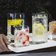 Modern rectangular clear glass highball glasses set with frosted edges filled with ice and colorful fruit garnishes