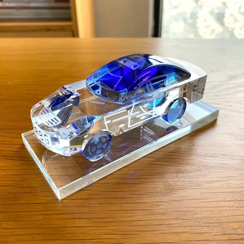 A sleek transparent crystal car model with vibrant blue tinted roof and wheels for modern office table decor