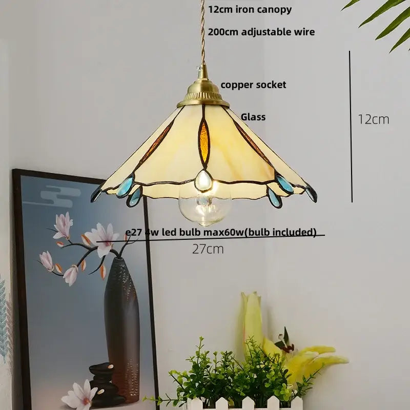 A tiffany-style pendant light with brass canopy and stained glass shade featuring cream amber and teal accents suspended by copper wire