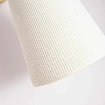 A sleek white cylindrical decorbites ceramic led wall light with vertical ribbed texture and brass pull chain for bedroom decor