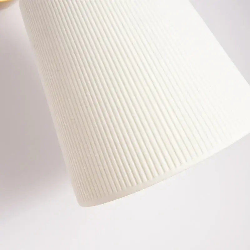 A sleek white cylindrical decorbites ceramic led wall light with vertical ribbed texture and brass pull chain for bedroom decor