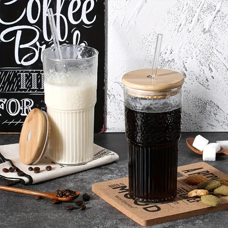 Modern ribbed glass cup with bamboo lid and clear straw filled with dark coffee in a tall ribbed glass tumbler