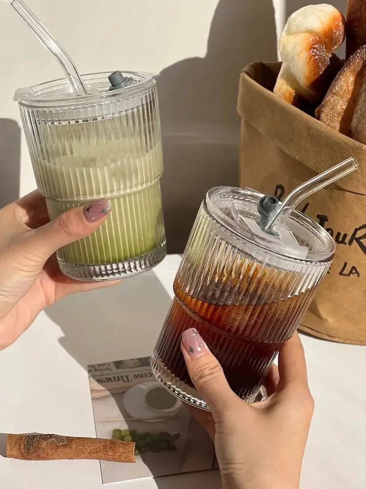 Two clear ribbed stripe glass cups with lids and straws, one filled with green iced tea and the other with dark iced coffee