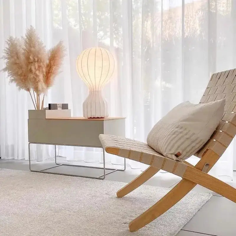 Modern ribbed white ceramic silk table lamp displayed next to a light beige woven wood lounge chair with striped cushion