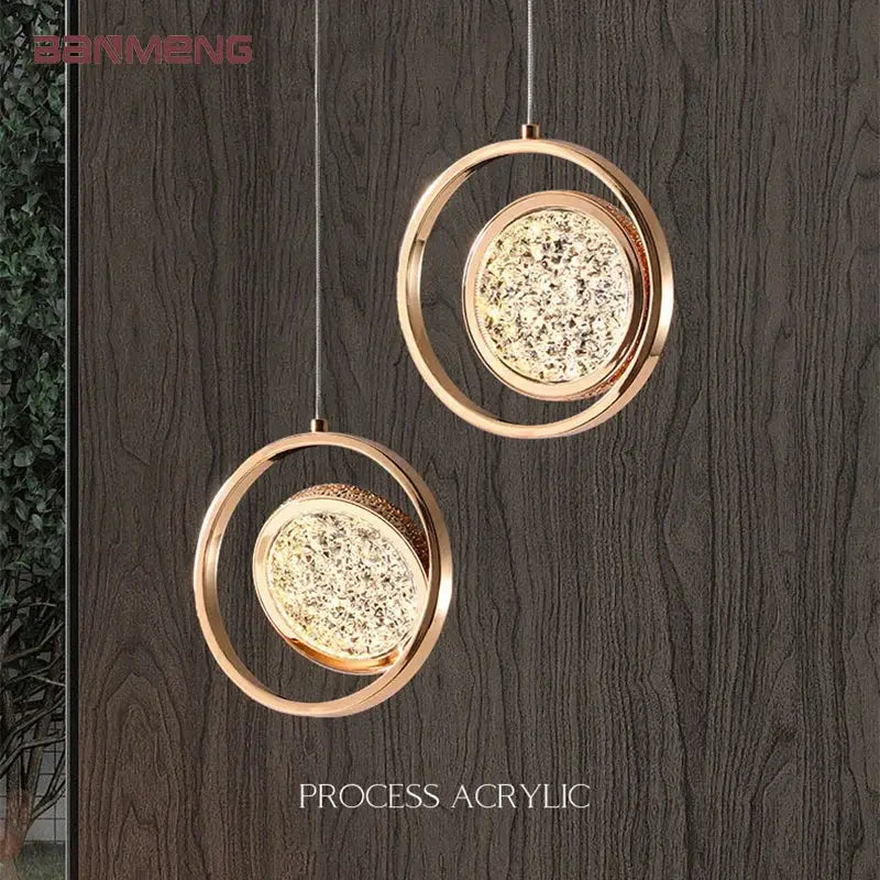 Two elegant rose gold acrylic led pendant lights with sparkling diffusers hang on a dark wood textured wall