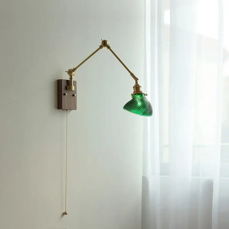 Modern rotatable brass wall light fixture with green ribbed glass shade mounted on articulated arm with wooden base and pull chain