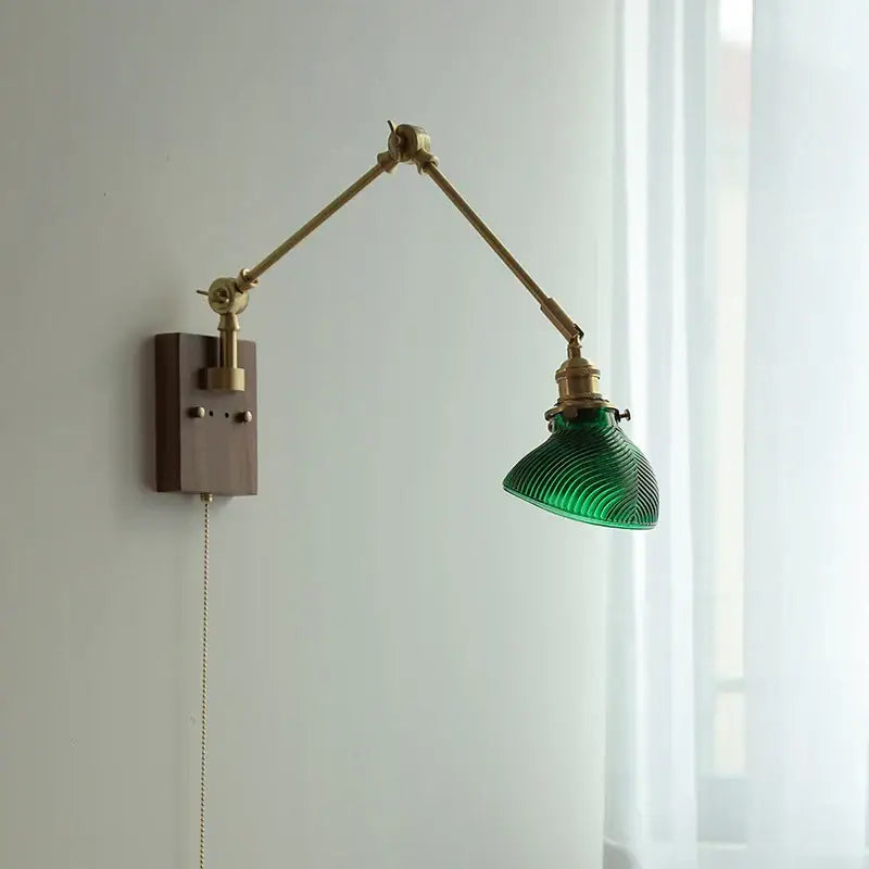 Modern rotatable brass wall light fixture with adjustable brass arms and textured green glass shade on dark wood base
