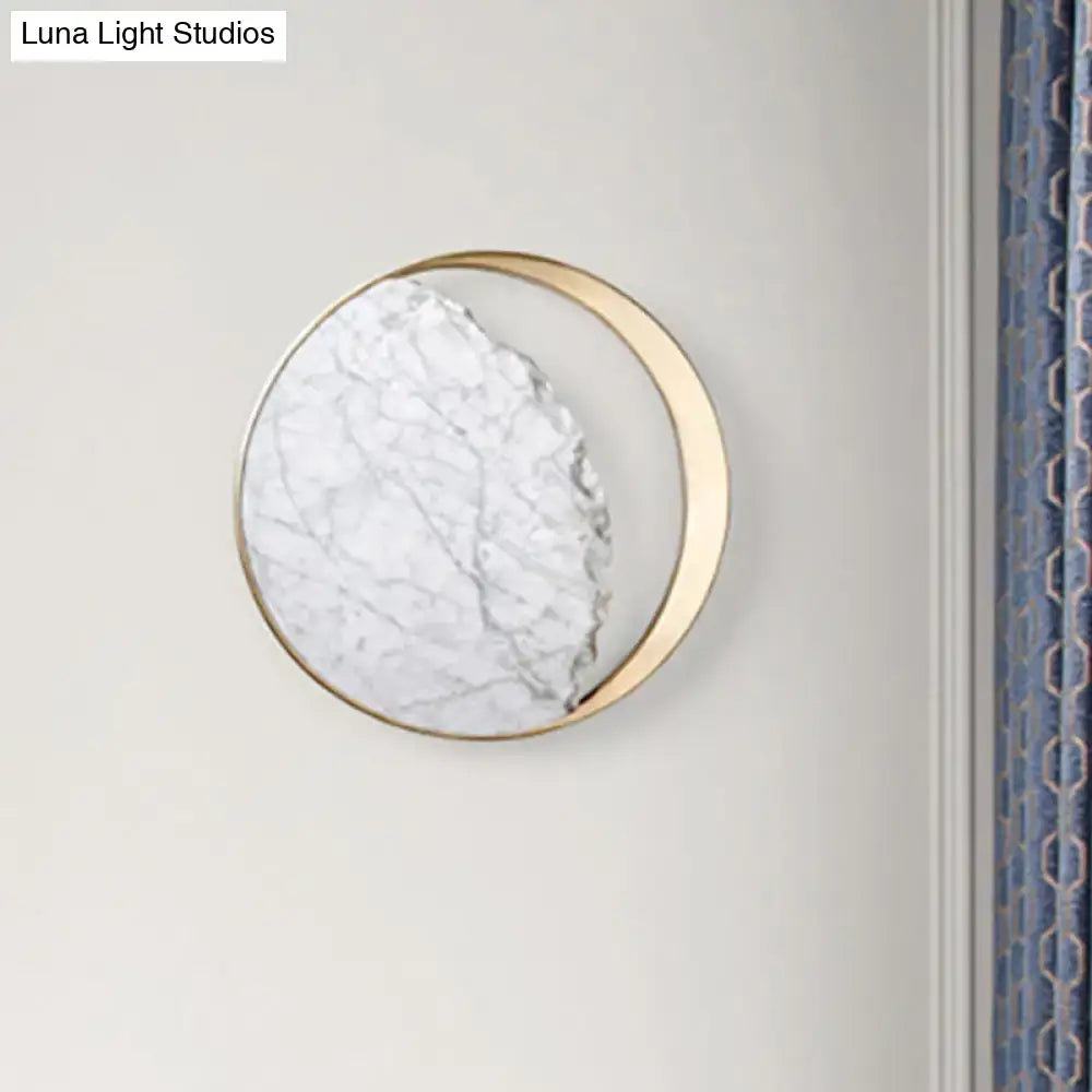 A modern round gold and white marble led wall sconce with a gold-toned metallic frame for bedroom use