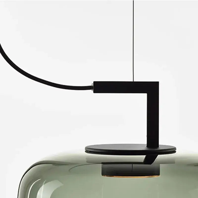 Black metal arm and base supporting a translucent olive green glass pendant lamp in a modern dining room set of 3
