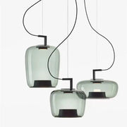 Three modern pendant lamps with translucent sage green glass pendant shades and black metal fixtures for dining room use