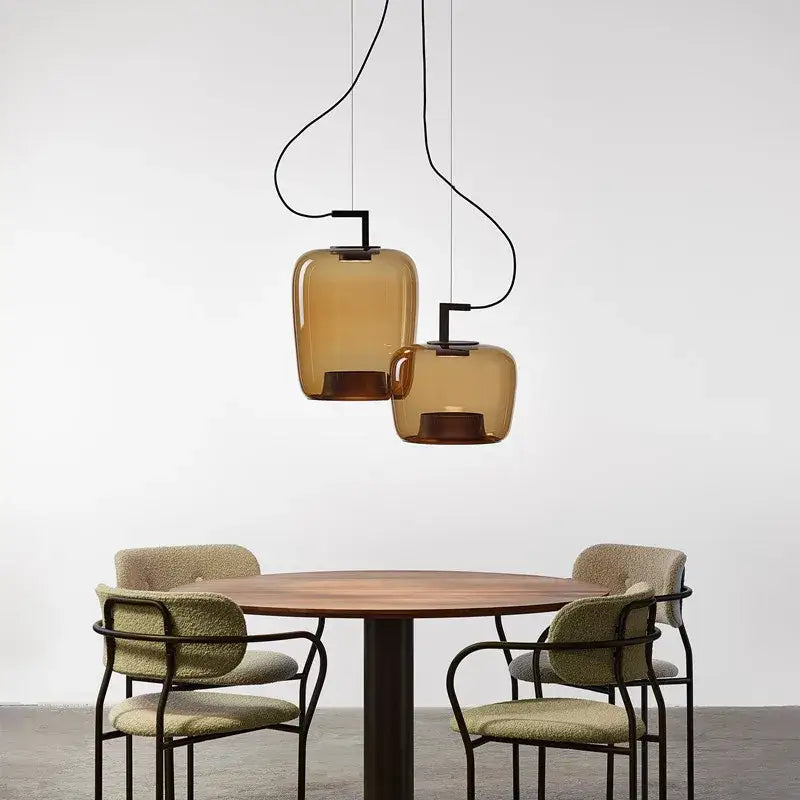 Two amber glass pendant lamps with black metal fixtures hang above a wooden table in a modern dining room set