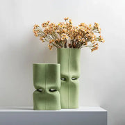 Two matte sage green hollow ceramic vases with sculpted face designs for modern living room decor